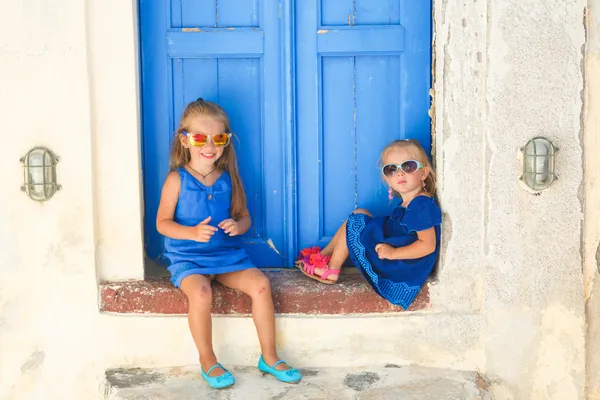 Hermanitas lindas sentadas cerca de la vieja puerta azul en el pueblo griego de Emporio, Santorini —  Fotos de Stock