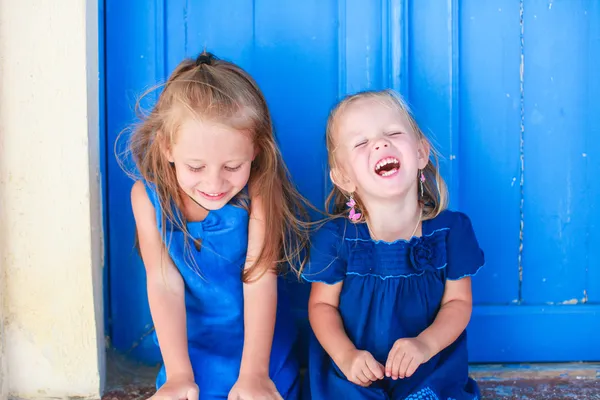 Retrato de niñas sonrientes sentadas cerca de la vieja puerta azul en el pueblo griego, Emporio, Santorini —  Fotos de Stock