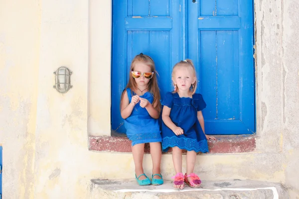 Μικρό χαριτωμένο αδελφές συνεδρίασης κοντά παλαιά μπλε πόρτα στο ελληνικό χωριό του Εμπορειού, Σαντορίνη — Φωτογραφία Αρχείου