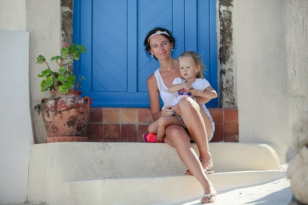 Junge mutter und ihre tochter sitzen vor der tür eines alten hauses in emporio dorf, santorini, griechenland — Stockfoto