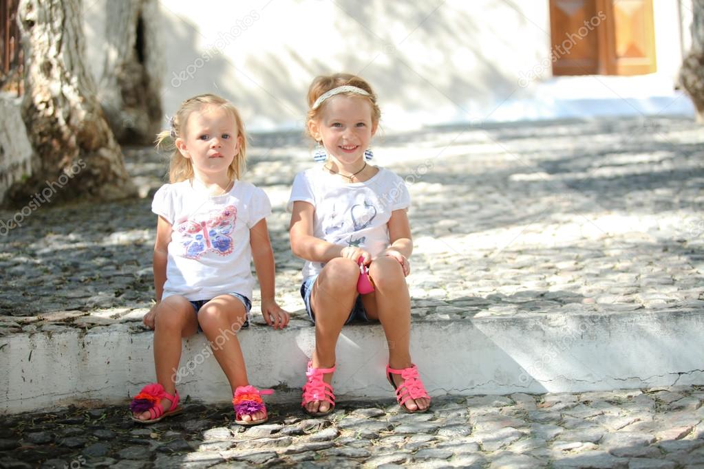 Little cute sisters sitting at street in old Greek village of Emporio, Santorini