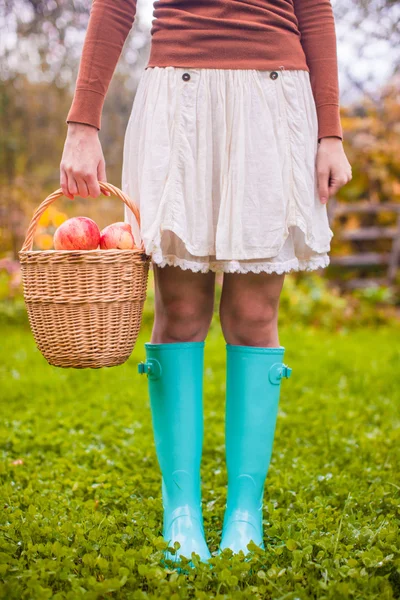 Close-up de cesta com amarelo, maçãs vermelhas e botas de borracha em uma jovem — Fotografia de Stock