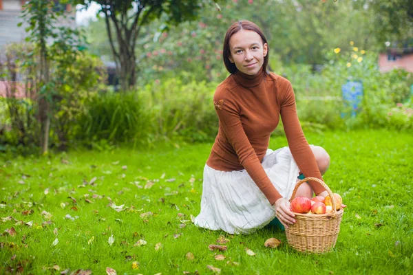 Mladá žena v gumové boty, držení proutěný koš s červenými jablky na podzim — Stock fotografie