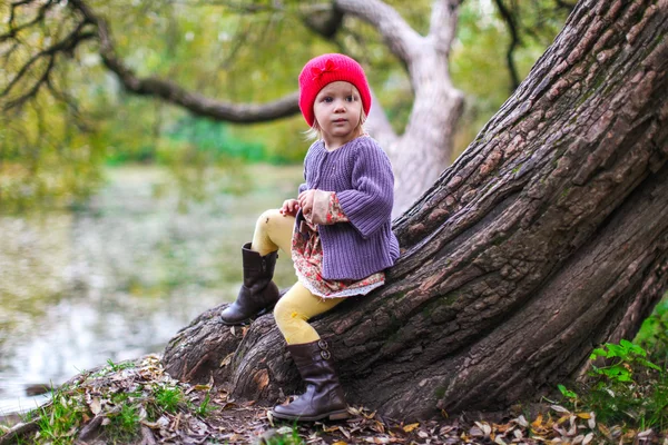 Söt liten flicka i en röd mössa nära sjön på hösten park — Stockfoto