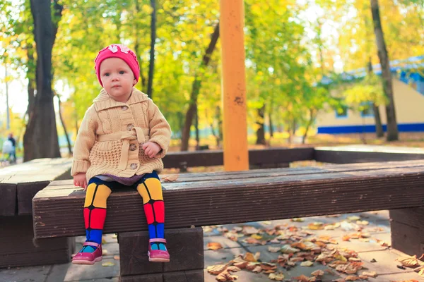 थोडे सुंदर मुलगी शरद ऋतू पार्क मध्ये एक खंडपीठावर बसतो — स्टॉक फोटो, इमेज