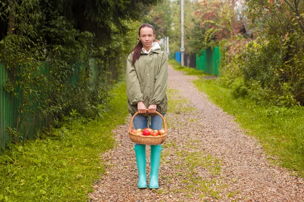 Jeune femme en bottes en caoutchouc avec panier de pommes dans les mains à l'automne — Photo