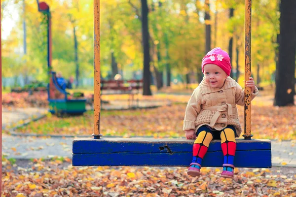 Liten vacker flicka att ha kul på en gunga i parken hösten — Stockfoto