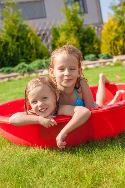 Två söta lilla glada tjejer ha kul i liten pool på gården utomhus och njuta av sin semester — Stockfoto