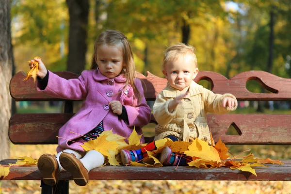 Two little beautiful girls sitting on the bench in warm autumn day — Stock Photo, Image