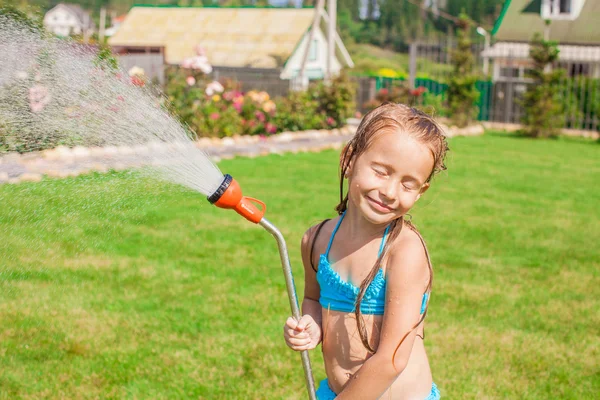 Adorable niña feliz vertiendo agua de una manguera y riendo — Foto de Stock