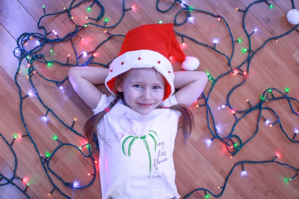 Pequena menina feliz encontra-se entre as luzes multi-coloridas em um piso de madeira — Fotografia de Stock