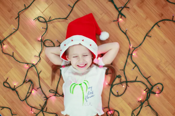 Little happy girl lies among the multi-colored lights on a wooden floor — Stock Photo, Image