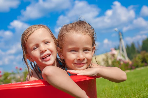 Dos lindas niñas felices divirtiéndose en una pequeña piscina en el patio al aire libre y disfrutar de sus vacaciones —  Fotos de Stock