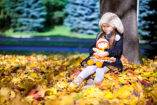 Pretty Fashion girl sits under a maple tree with doll on sunny autumn day — Stock Photo, Image