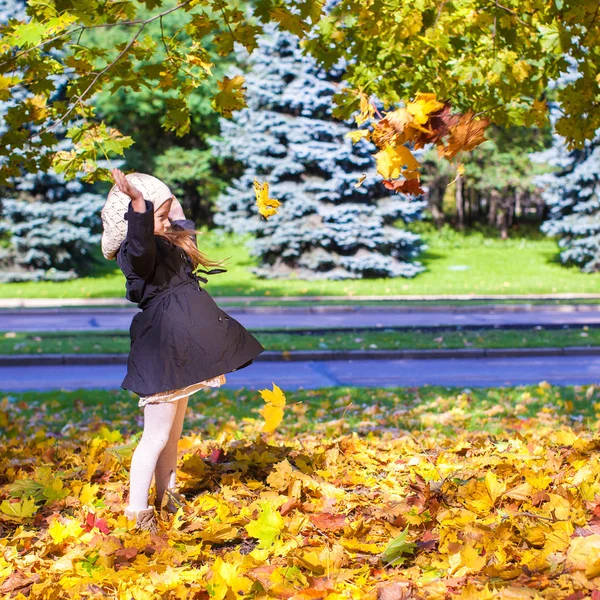 Piccola ragazza divertente lancia foglie autunnali nel parco in una giornata di sole autunnale — Foto Stock