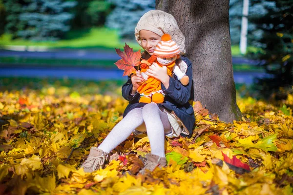 Hübsches Mode-Mädchen sitzt unter einem Ahornbaum mit Puppe und rotem Blatt an einem sonnigen Herbsttag — Stockfoto