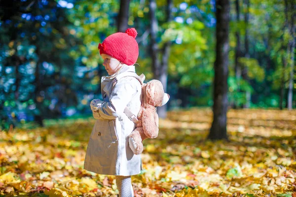 Kleines Mädchen mit Rucksack-Bär spaziert an schönem sonnigen Tag durch den Herbstwald — Stockfoto