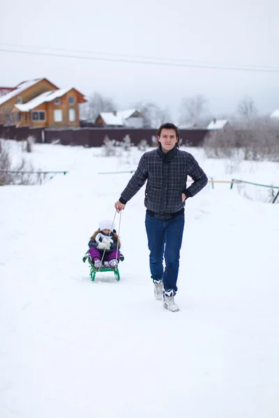 Young dad rolls his little cute daughter on a sled in the snow outdoors — Stock Photo, Image