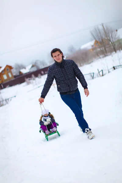 Young dad rolls his little cute daughter on a sled in the snow outdoors — Stock Photo, Image