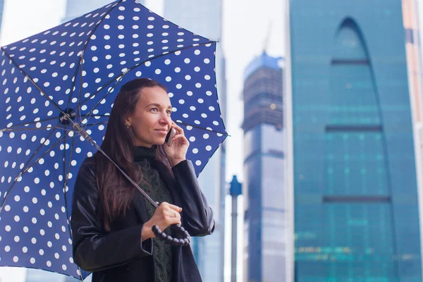 Jóvenes mujeres de negocios encantadoras hablando por teléfono bajo un paraguas en un día lluvioso —  Fotos de Stock