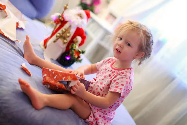 Liten bedårande flicka tidigt på morgonen öppnar julklappar — Stockfoto