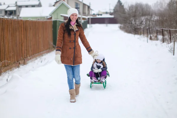 Ung mamma rullar sin lilla söta döttrar på en släde i vinterdag — Stockfoto