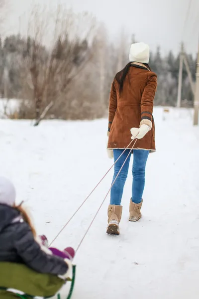 Vue arrière de la jeune mère roule ses petites filles mignonnes sur un traîneau en journée d'hiver — Photo