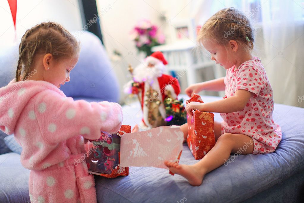 Two charming little sisters early in the morning opening Christmas gifts