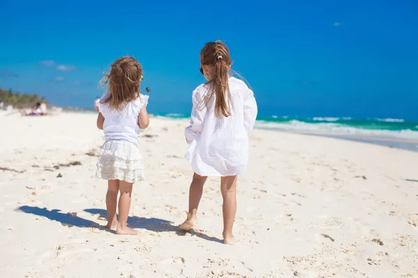 Vista posteriore di due sorelline in abiti bianchi che si divertono sulla spiaggia di sabbia tropicale — Foto Stock