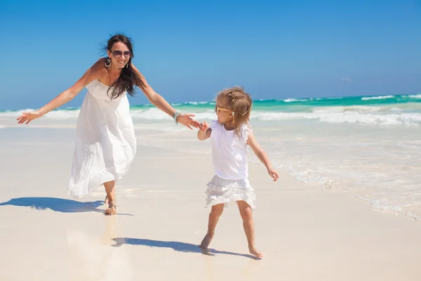 Young beautiful mother with her adorable little daughter running on white beach — Stock Photo, Image