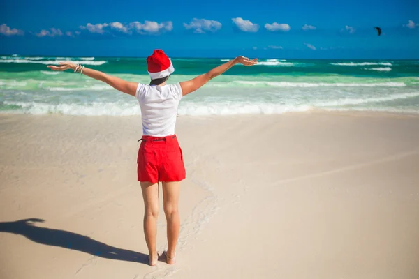 다시 보기 산타 모자 걷고 있는 젊은 여자의 하얀 해변에 그녀의 손을 확산 — 스톡 사진