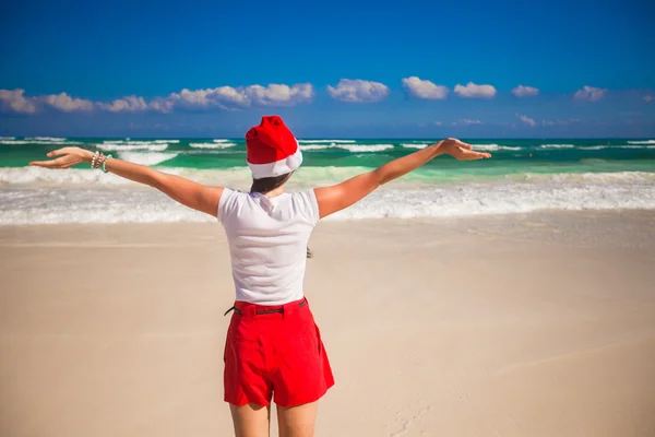 Jonge vrouw in Kerstman hoed wandelen verspreiden haar handen op witte zandstrand — Stockfoto