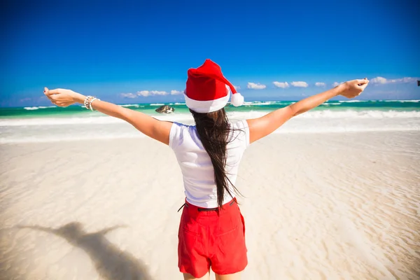 Vista posteriore di bella ragazza in cappello di Babbo Natale a piedi come un uccello sulla spiaggia bianca — Foto Stock