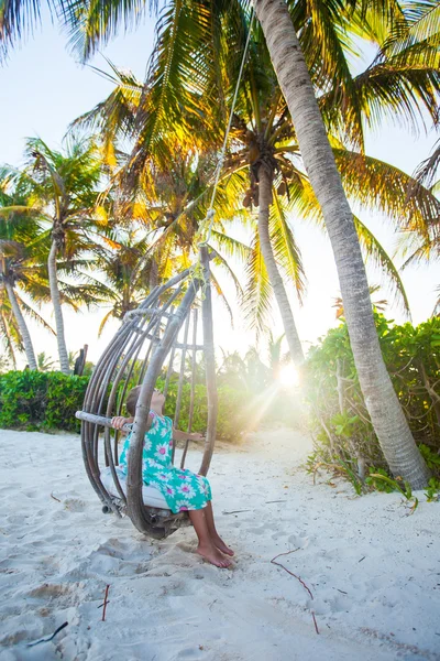 Adorable niña en un vestido y gafas de sol en swing en la playa caribeña de arena blanca —  Fotos de Stock