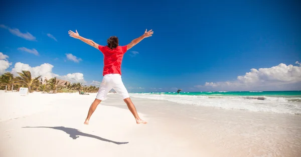 Young man jumping and raising his arms up on the beach — Stock Photo, Image
