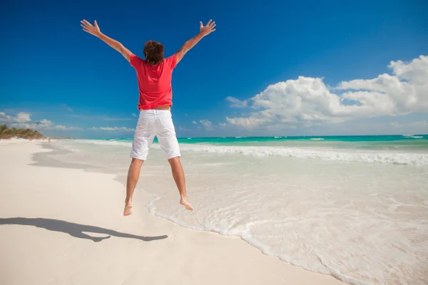 Giovane uomo che salta e alza le braccia sulla spiaggia di fagioli — Foto Stock