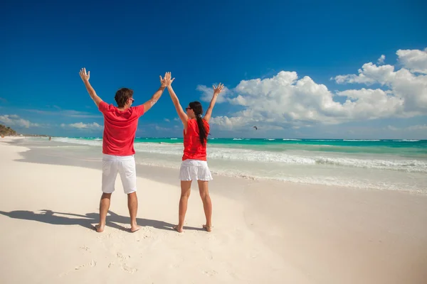 Вид ззаду молода пара розтягнула руки, стоячи на білому піщаному пляжі — стокове фото