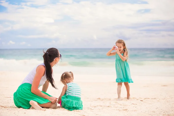 Маленькая девочка фотографирует свою мать и младшую сестру на пляже — стоковое фото