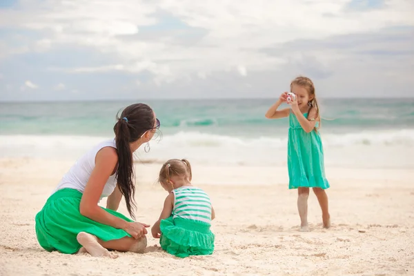 Маленькая девочка фотографирует свою мать с сестрой на пляже — стоковое фото