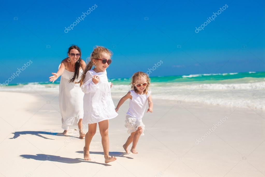Young happy mother and her adorable daughters having fun at exotic beach on sunny day