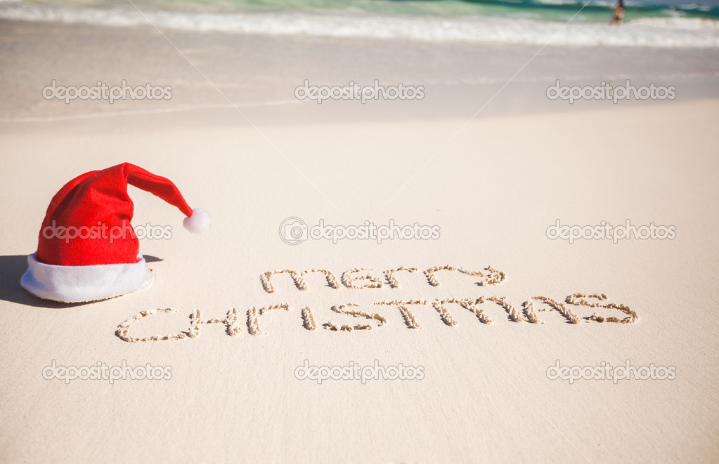 Santa Hat on white sandy beach and Merry Christmas written in the sand