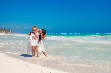 Genç annesi ile Meksika beyaz kumlu plajda oynayan küçük komik kızı