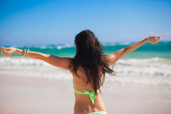 Rückansicht einer entzückenden jungen Frau, die den Urlaub genießt, breitet ihre Hände an einem weißen, tropischen Strand aus — Stockfoto