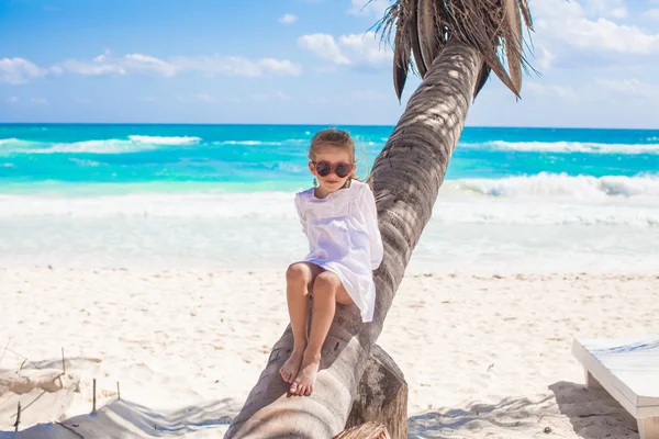 Little cute girl sitting on palm tree at the perfect caribbean beach — Stock Photo, Image