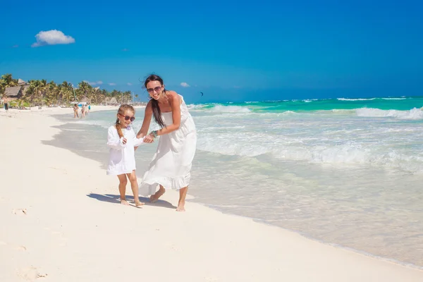Маленькая забавная дочь играет со своей молодой матерью на белом песчаном пляже в Мексике — стоковое фото