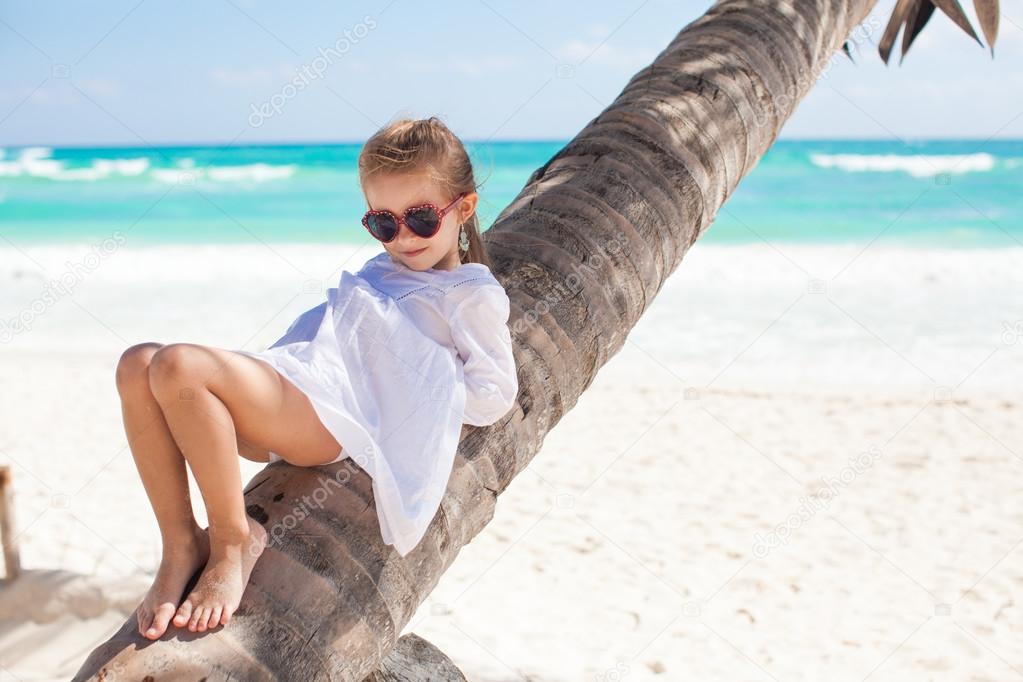 Portrait of little cute girl sitting on palm tree at the perfect caribbean beach