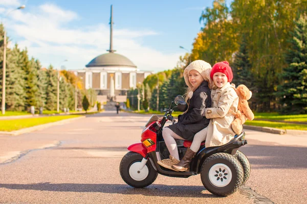 Twee kleine mooie zusters zittend op speelgoed motorfiets in herfst park — Stockfoto