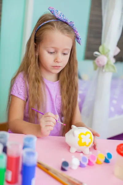 Маленькая девочка рисует сидя за столом в комнате на заднем плане ее комнаты — стоковое фото
