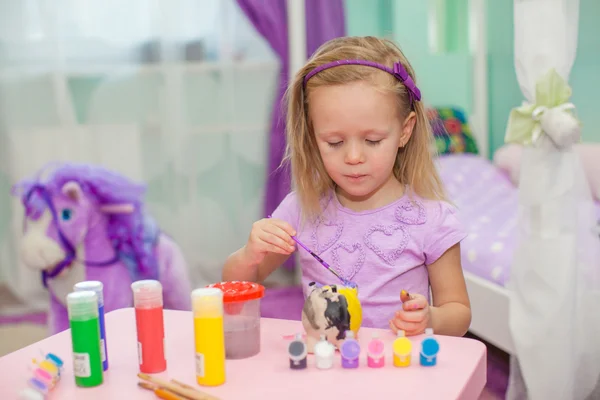 Маленькая красивая девочка рисует краски на столе — стоковое фото