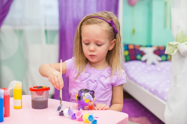 Маленькая девочка рисует краски на своем столе в комнате — стоковое фото